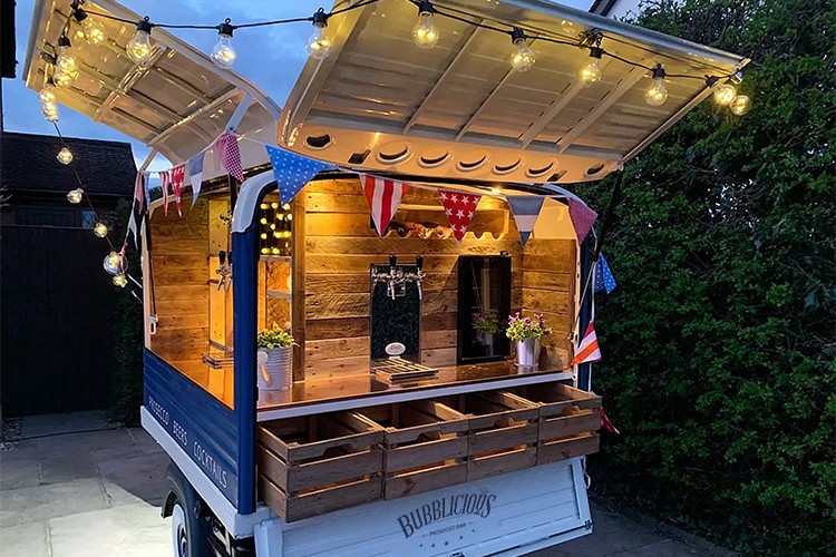 Rear shot of a customised blue and white Bubblicious branded lit up Tuk Tuk with lightbuls and flags around