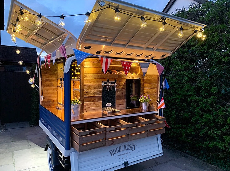 Rear shot of a customised blue and white Bubblicious branded lit up Tuk Tuk with lightbuls and flags around