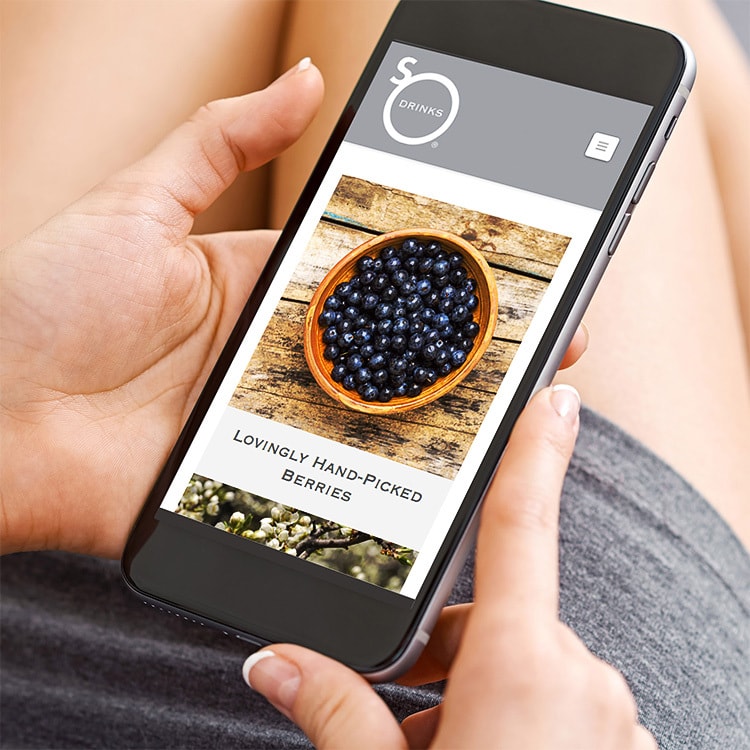 A person holding a mobile phone viewing the So Drinks responsive eCommerce website design