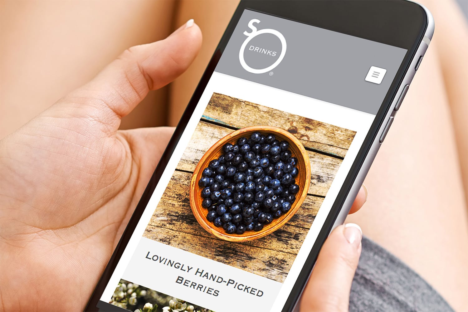 A person holding a mobile phone viewing the So Drinks responsive eCommerce website design