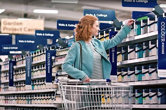 A woman holding a trolley and picking a paint bucket photography for Wickes