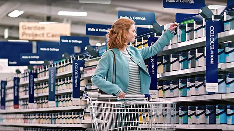 A woman holding a trolley and picking a paint bucket photography for Wickes
